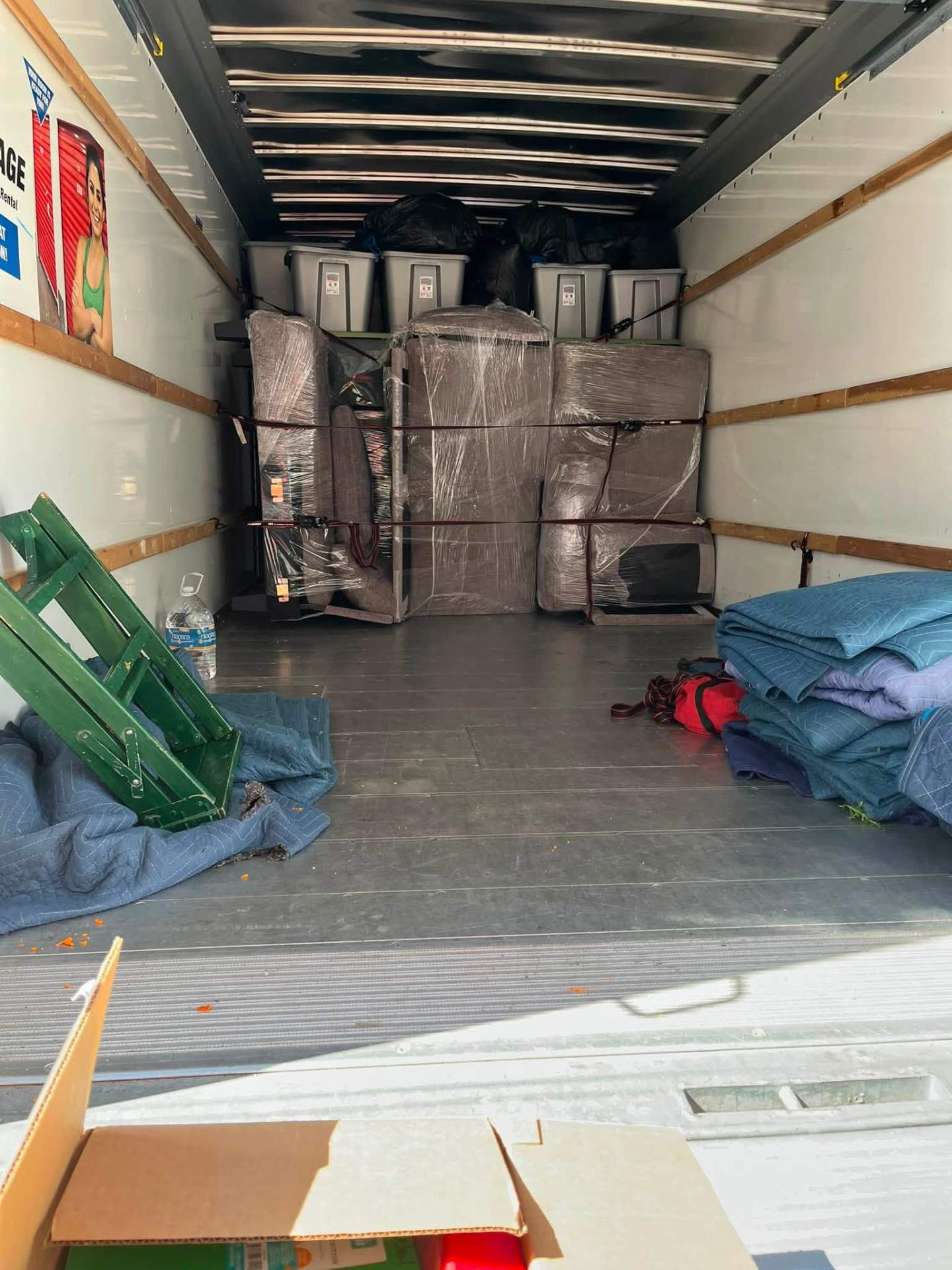 Sofa strapped upright with moving blankets on the floor